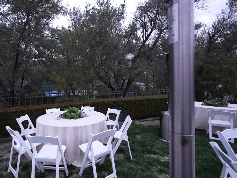 White linen round table and folding chairs set under oaks in a Castro Valley backyard