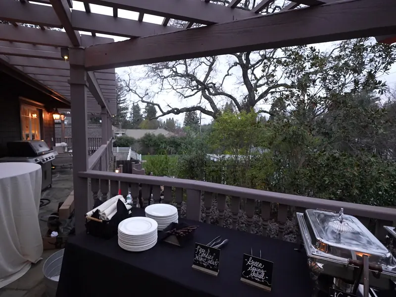 Chafing-dish buffet and plate setup under a patio pergola at dusk in Union City
