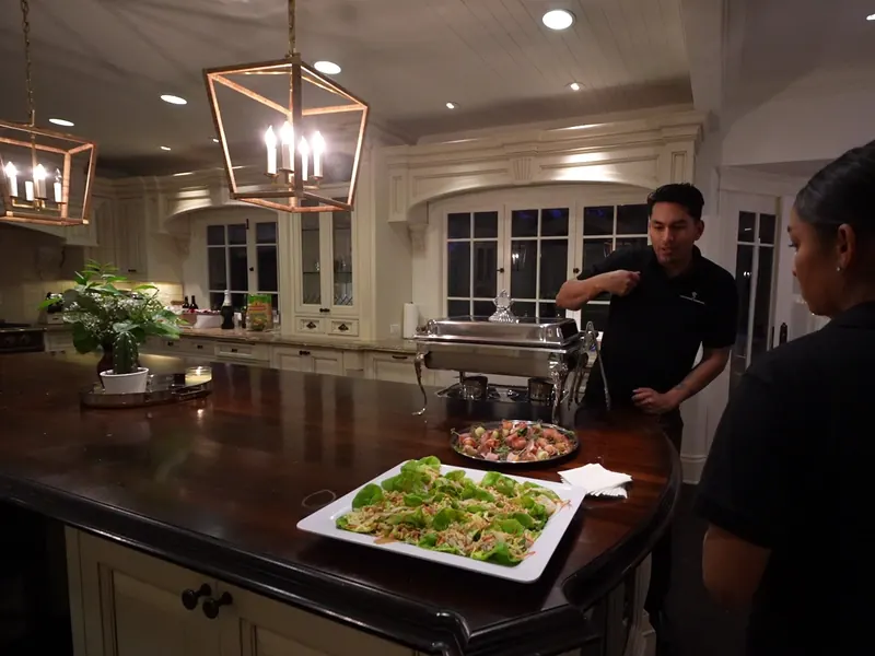 Server plating fresh salad platters on a kitchen island before a Castro Valley event