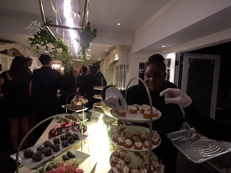 Server carrying a tray past a tiered dessert display at a Newark reception