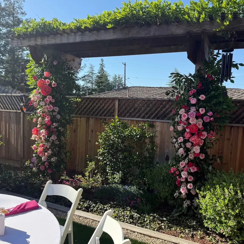 Medium floral arch installation in pink and red roses cascading over a wooden pergola with greenery