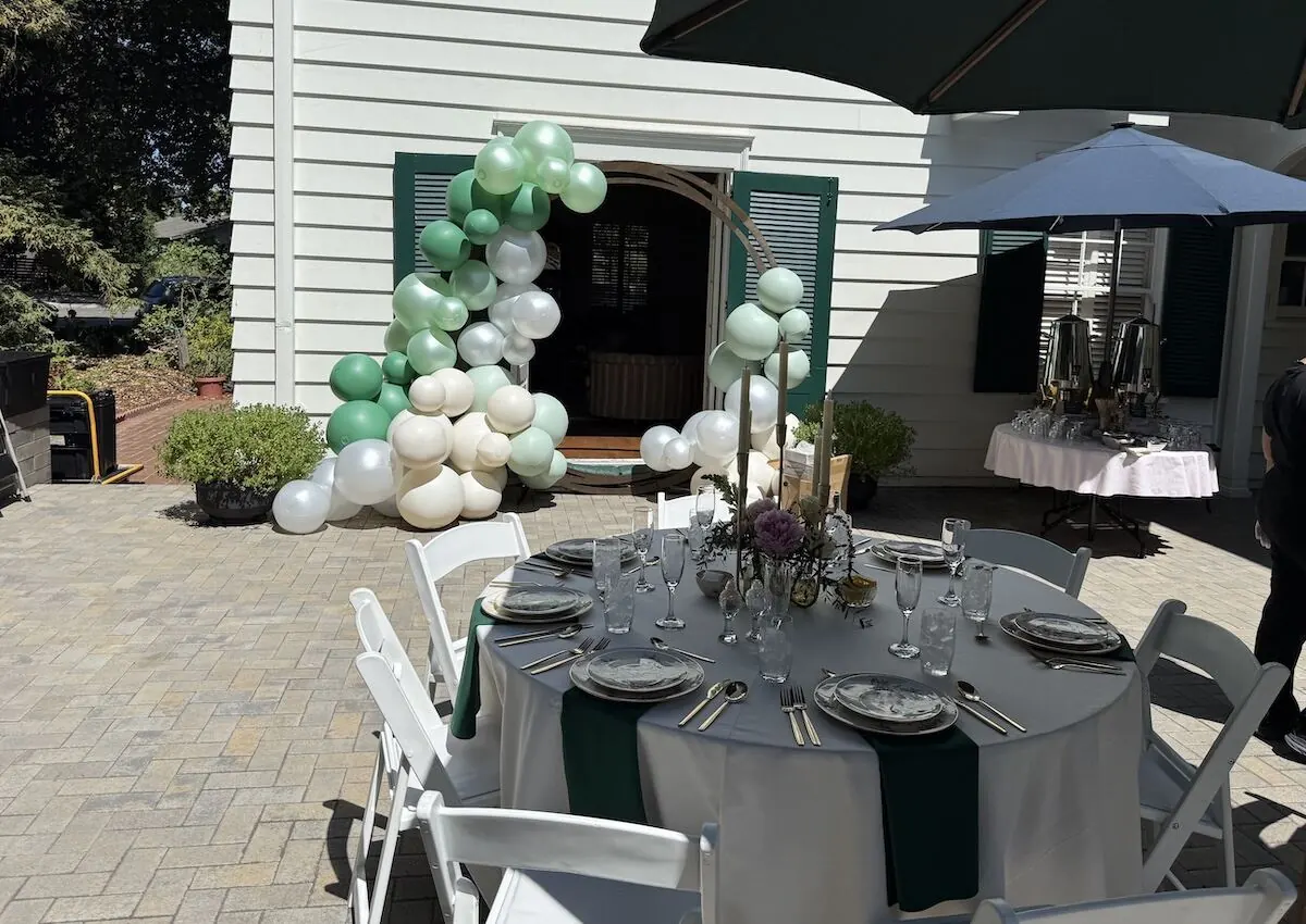 Sage and ivory balloon garland framing an archway beside a fully styled table — balloon and bloom styling from Fremont and Newark catering