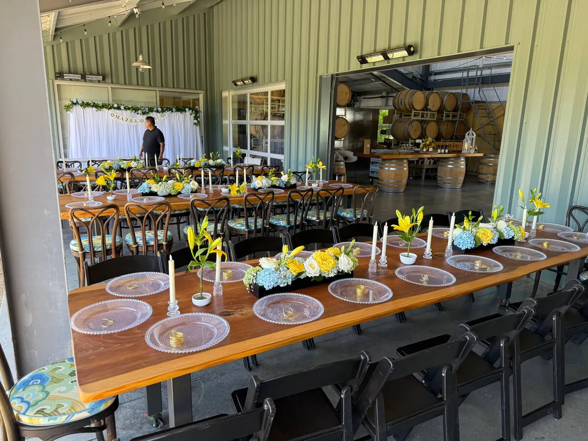 Long table with yellow lily, blue hydrangea, and white rose centerpieces with taper candles at a Fremont-area venue